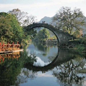 Ancient stone bridge reflected in Yulong River with people walking on top