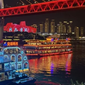 Night view of brightly lit cruise ships under the red bridge on the Two Rivers Night Cruise